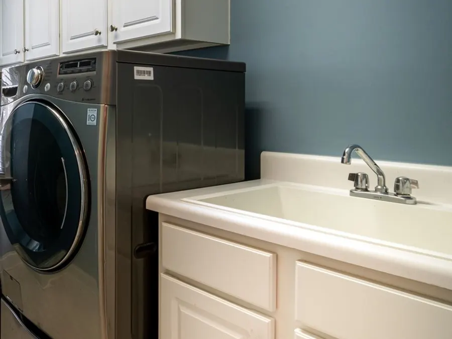Laundry room utility sink with white cabinets below a window