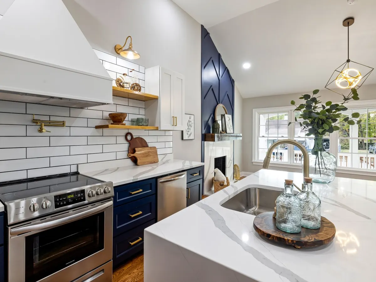 Kitchen with navy blue cabinets, white quartz waterfall island, and brass hardware