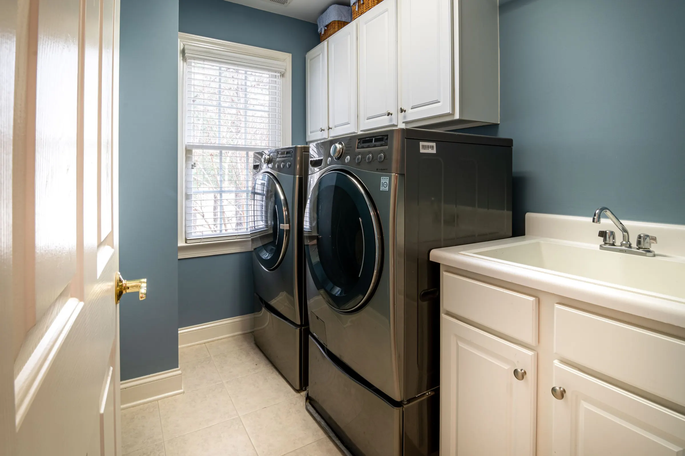 Laundry room with front-load machines, white upper cabinets, and a utility sink